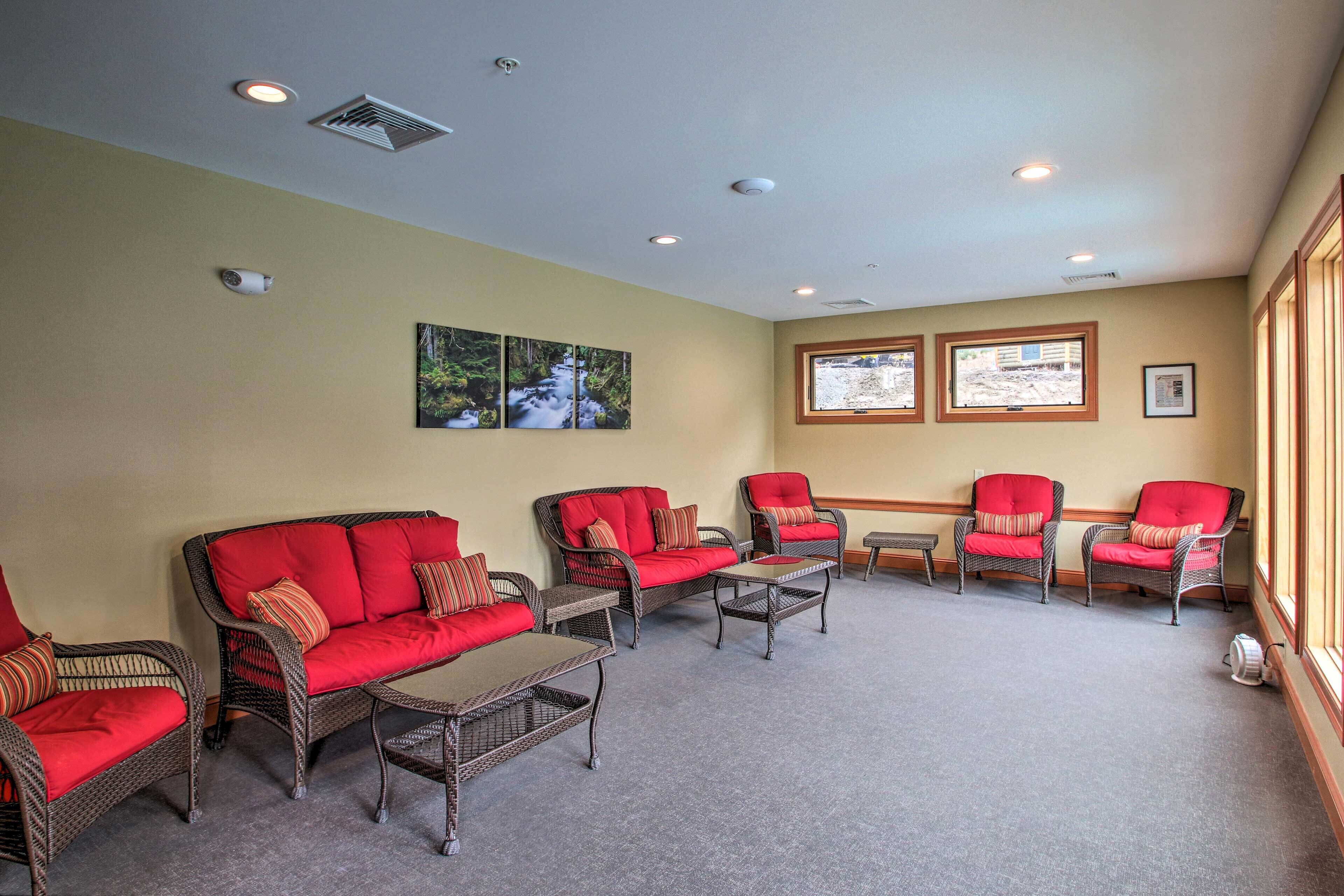A room with wicker furniture, red cushions, and two windows with views.