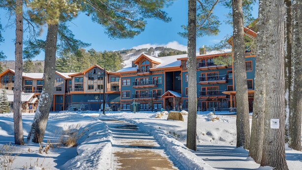 Eine Lodge mit mehreren Etagen und Balkonen, eingebettet in eine verschneite Landschaft mit Bäumen.