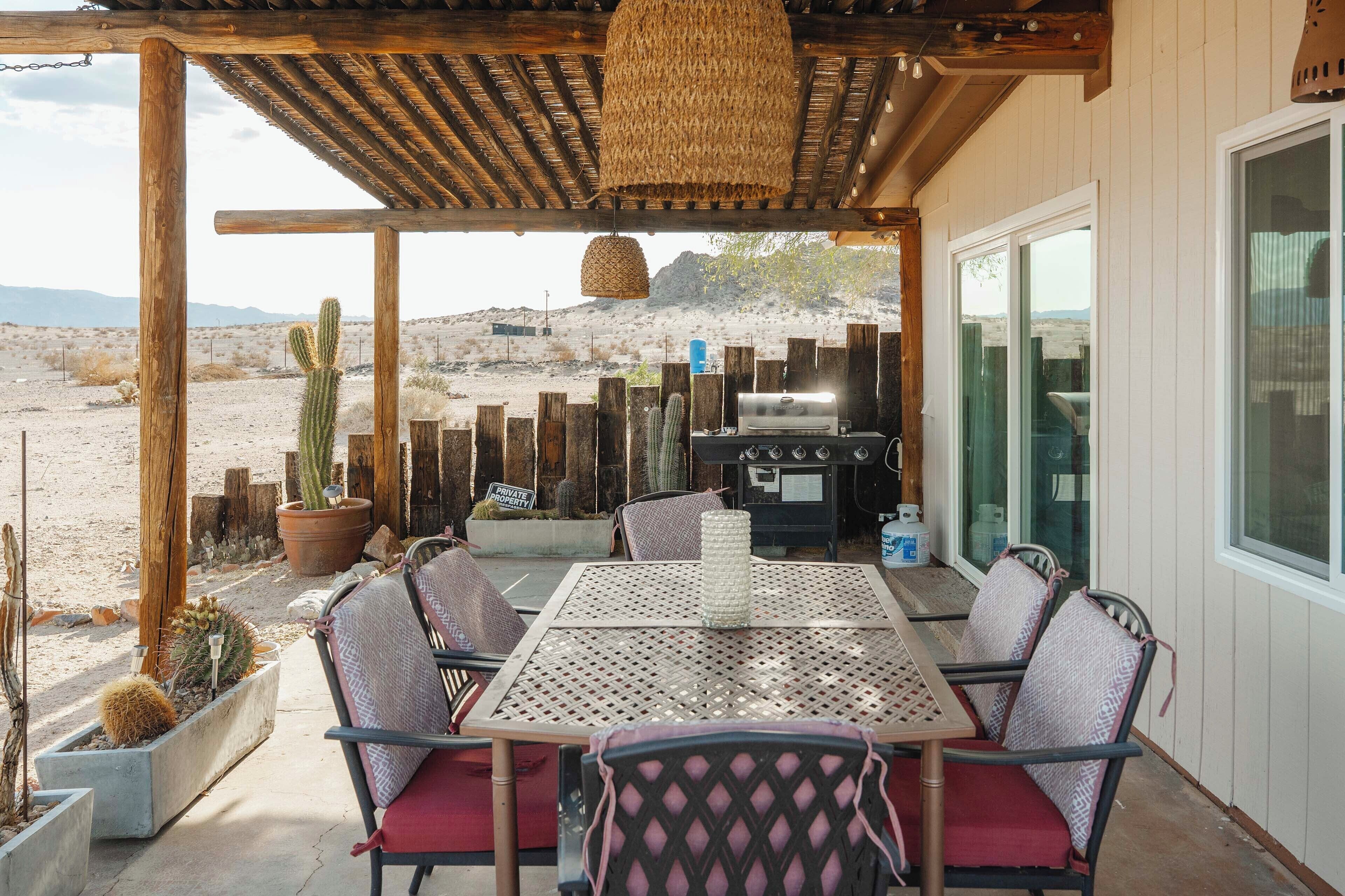 Un patio al aire libre con mesa y sillas, una parrilla y cactus.
