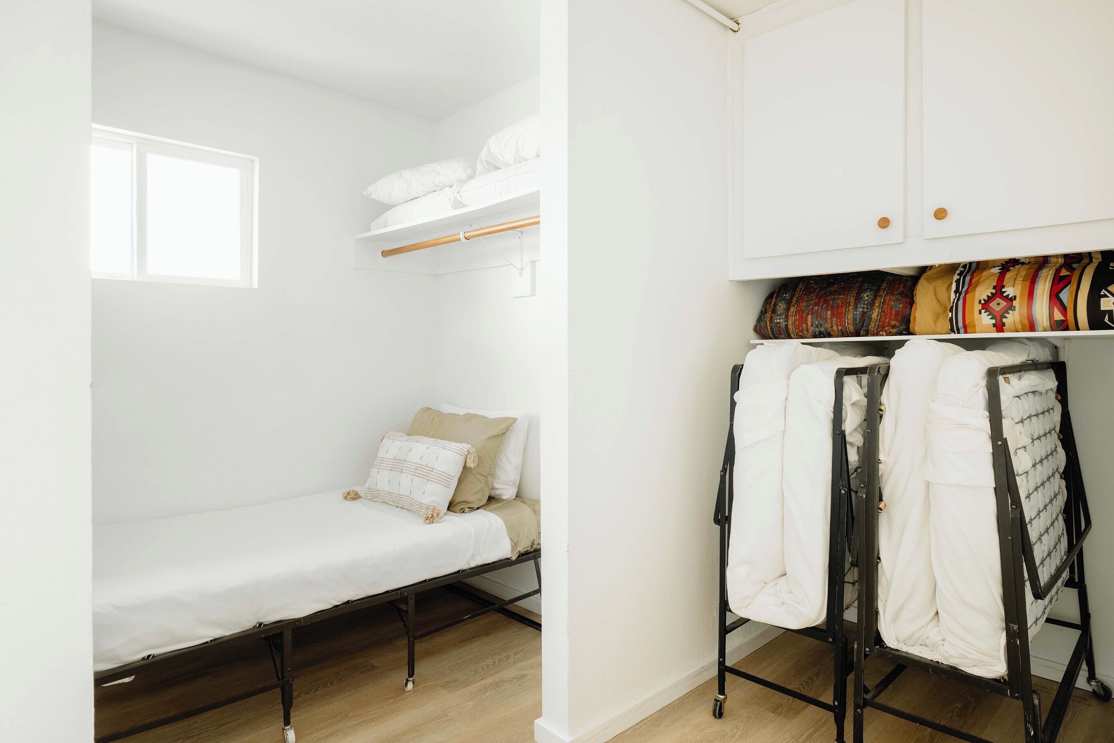 A small, white room with a bunk bed, a wardrobe, and a window.