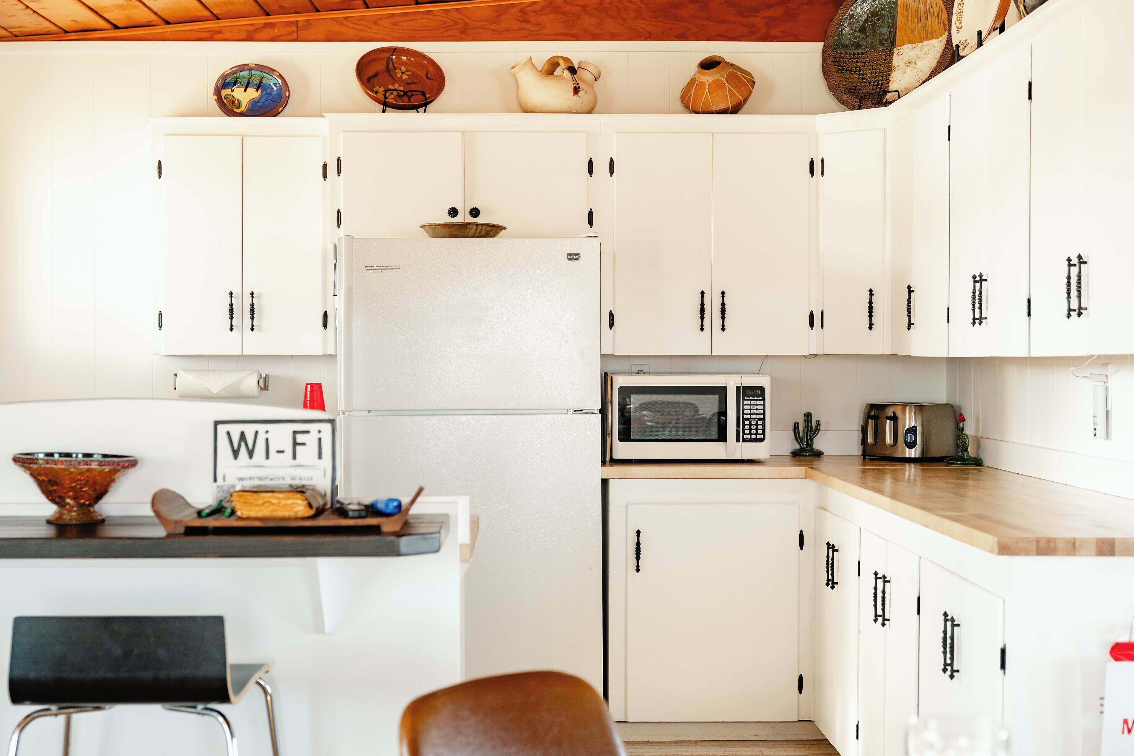 Eine kompakte Küche mit weißen Schränken, einer Mikrowelle, einem Toaster und einem WLAN-Symbol.