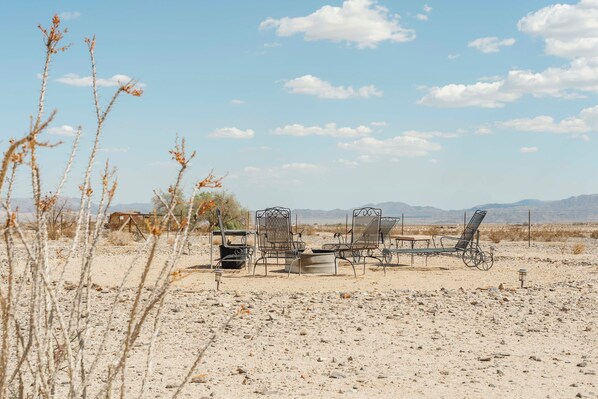 A desert landscape with a metal table and chairs, a small building, and sparse vegetation. - Twentynine Palms Desert Oasis w/ Pool & Hot Tub! (Twentynine Palms)