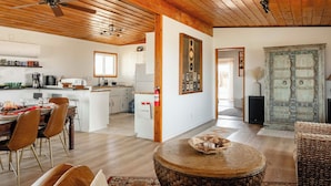Amplia sala de estar con techo de madera, una mesa de comedor con vajilla y un rincón de descanso acogedor con una mesa redonda.