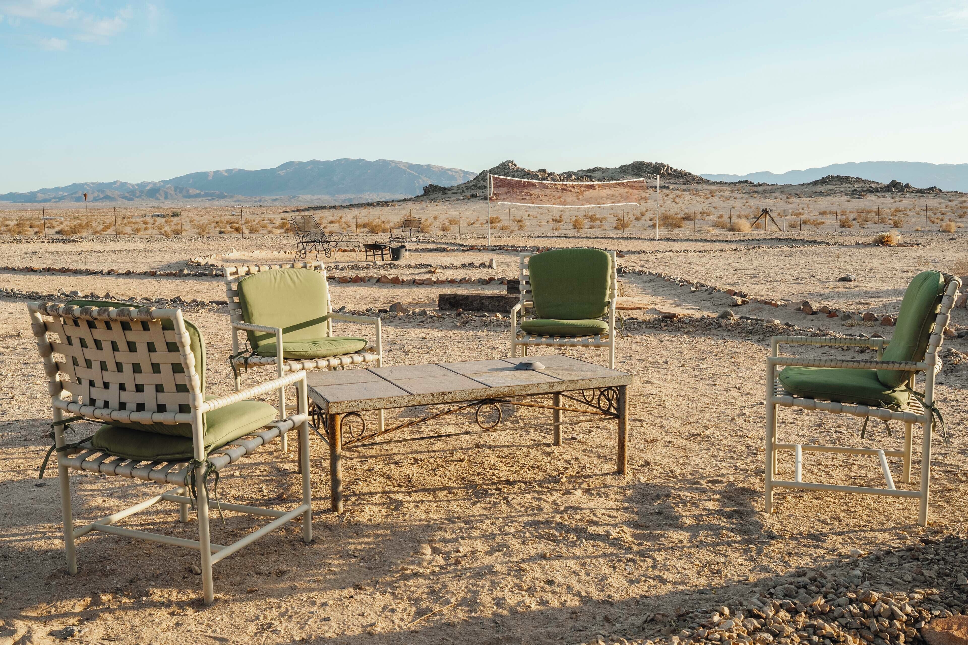 A desert setting with outdoor seating including metal chairs and a table, set against a backdrop of mountains.