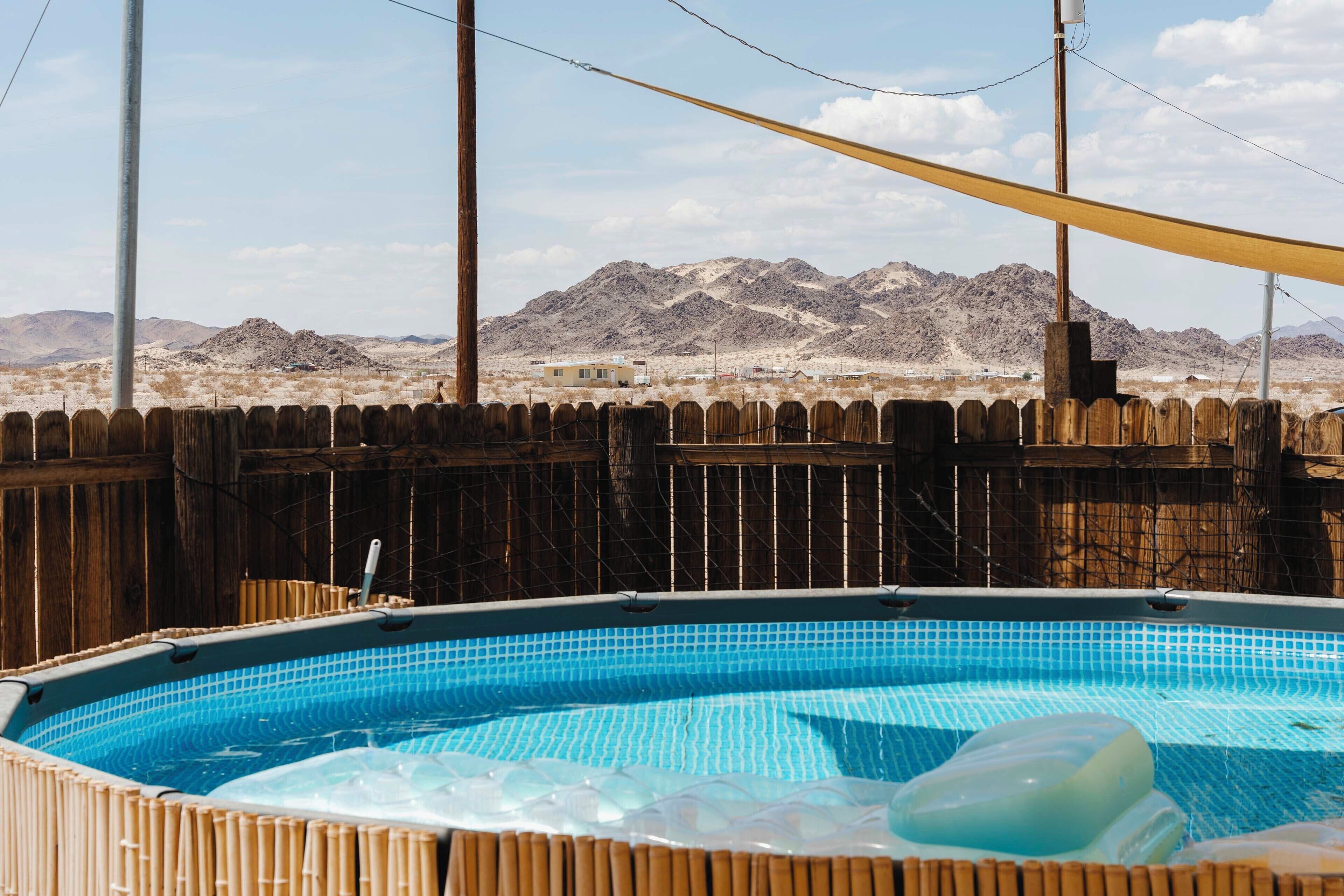 A swimming pool with a wooden fence and mountains in the background.