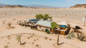 Un resort en el desierto con un edificio de una sola planta, paneles solares, una piscina y vegetación escasa.
