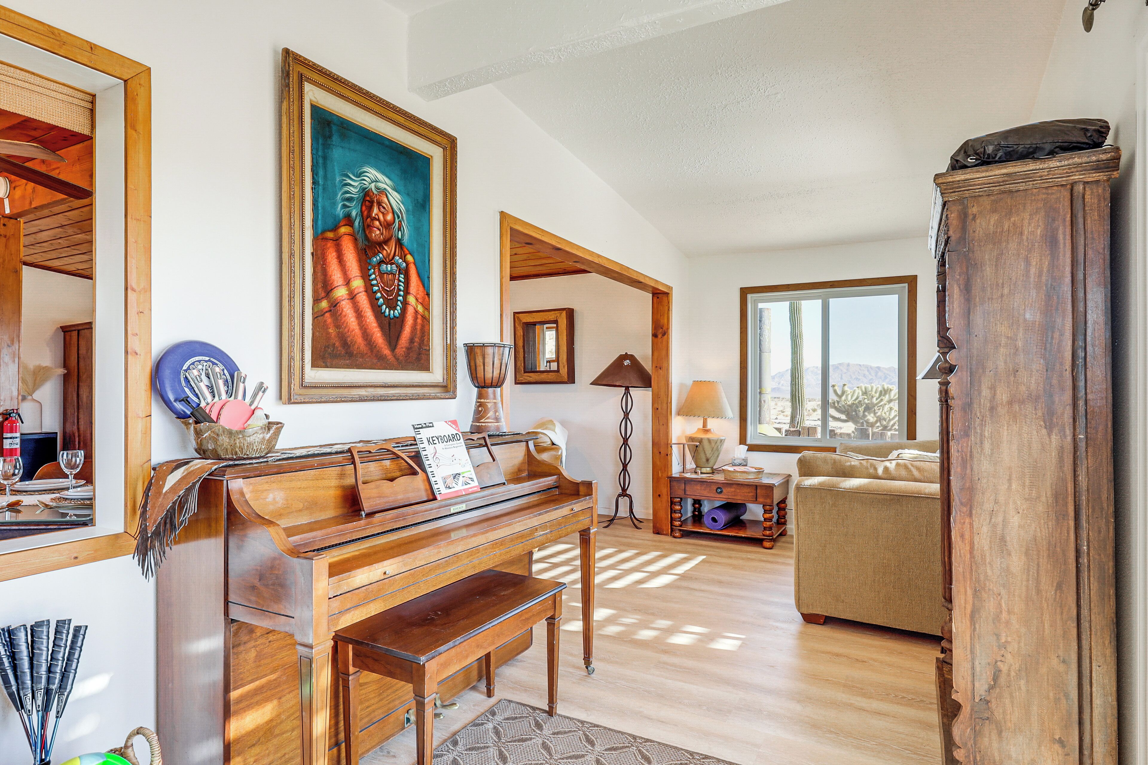 Ein Wohnzimmer mit einem Holz-Klavier, einer Couch, einem großen Gemälde und Bergblick durch ein Fenster.