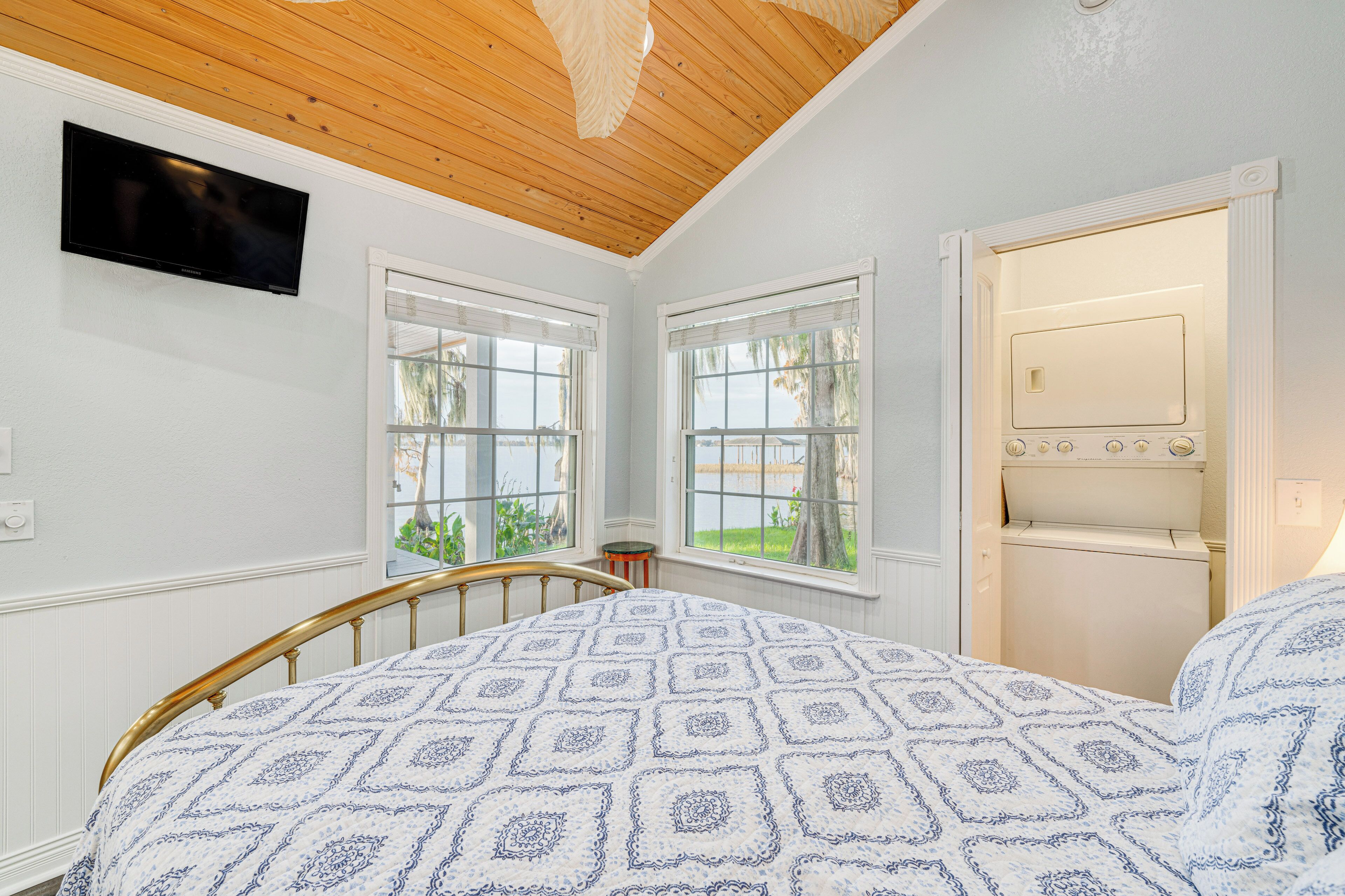 A bedroom with a bed, a television, two windows, and a door leading to a bathroom.