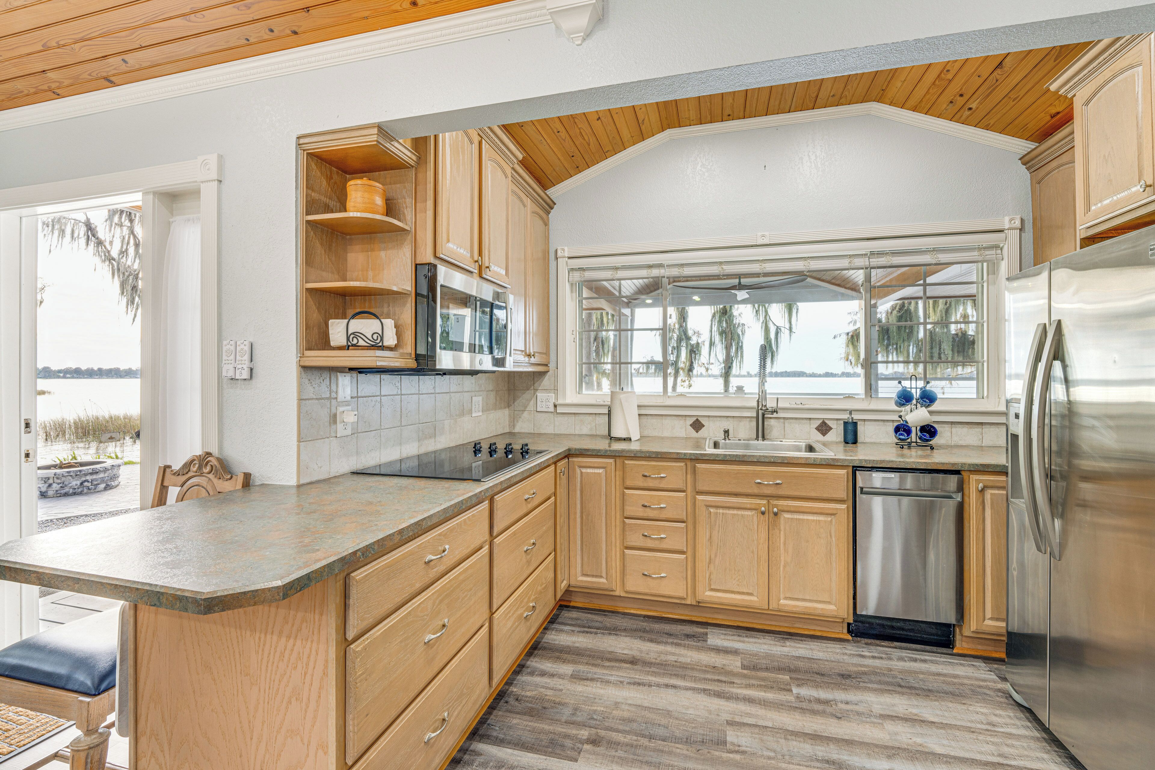 A kitchen with wooden cabinets, a stainless steel refrigerator, a dishwasher, and a large window overlooking a body of water.
