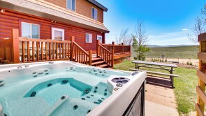 A wooden cabin with a hot tub and picnic table, surrounded by a deck and a view of the landscape.