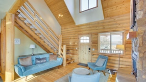 A log cabin interior with a wooden staircase, a blue sofa, a chair, and a stone fireplace.