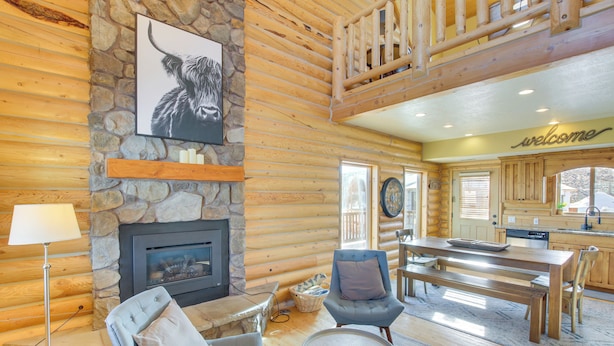 A log cabin interior with a stone fireplace, a dining area, and a cozy seating area.