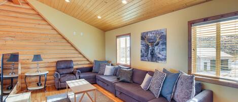 A cozy living room with a wooden ceiling, a sectional sofa, a coffee table, and a TV.