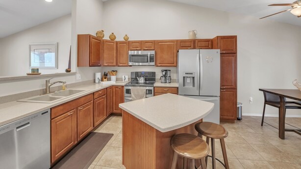 A modern kitchen with wooden cabinets, stainless steel appliances, and a central island with stools. - Summer All Year Round 2 Bedroom Home by RedAwning (Phoenix)