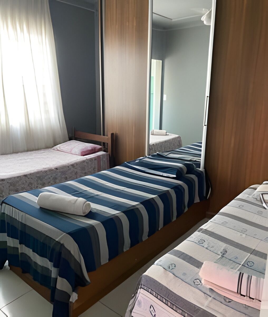 Une chambre avec deux lits, une armoire en bois, un miroir et une fenêtre avec des rideaux.