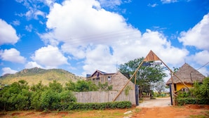A rural village with a thatched-roof house, a wooden fence, and a dirt path leading to a mountain.