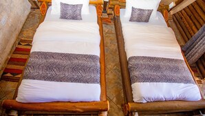 Two wooden beds with white linens and patterned pillows, a stone wall, and a tiled floor.