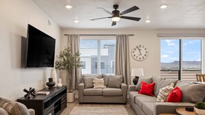 A living room with a sofa, a coffee table, a TV, and a large window with a view. - Desert Disney 2 Bedroom Condo (St. George)