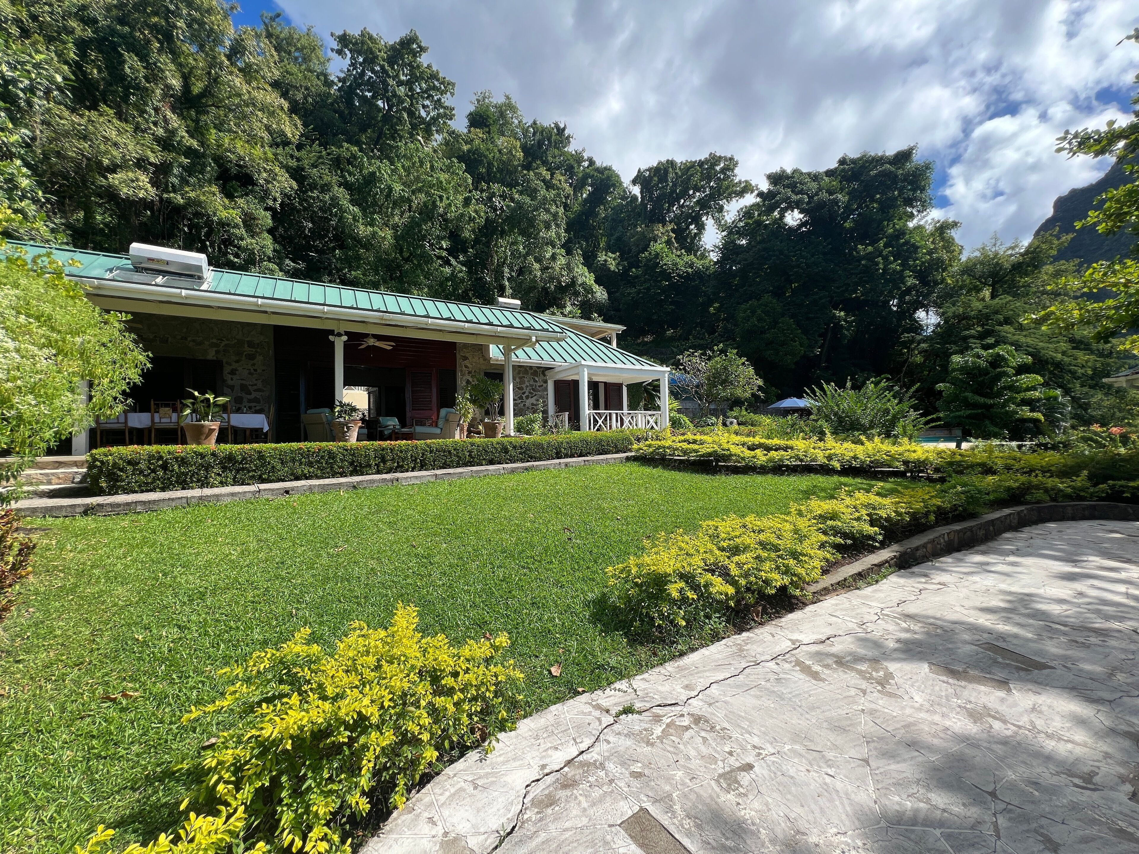 A building with a green roof, stone walls, and a covered porch with outdoor seating.