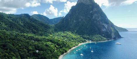 A coastal landscape with a prominent mountain, a beach, and several boats in the water.