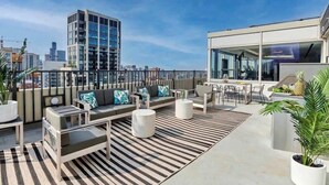 A rooftop terrace with a modern outdoor seating area, including sofas and tables, and a view of the city skyline. - Luxury Designer Penthouse 3802 | Pool | Gold Coast (Chicago)