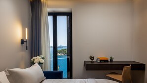 Een hotelkamer met een bed, een bureau, een stoel, een wereldbol, een boek en uitzicht op zee.
