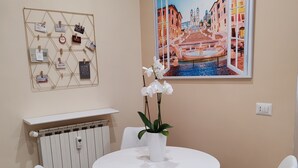 Une salle de bain moderne avec un lavabo blanc, deux chaises blanches, une table blanche et un tableau représentant un paysage urbain européen.