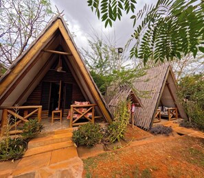Two wooden A-frame structures with a small porch area in front, surrounded by vegetation. - Boma Simba Lodge  (Voi)