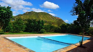 A rectangular swimming pool with a stone border, surrounded by lush greenery and a mountain in the background. - Boma Simba Lodge  (Voi)