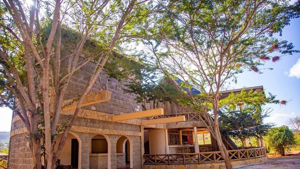 A stone building with arched doorways and a wooden balcony. - Boma Simba Lodge  (Voi)