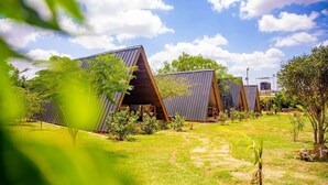 A row of modern, triangular-roofed cabins in a lush, green setting. - Boma Simba Lodge  (Voi)