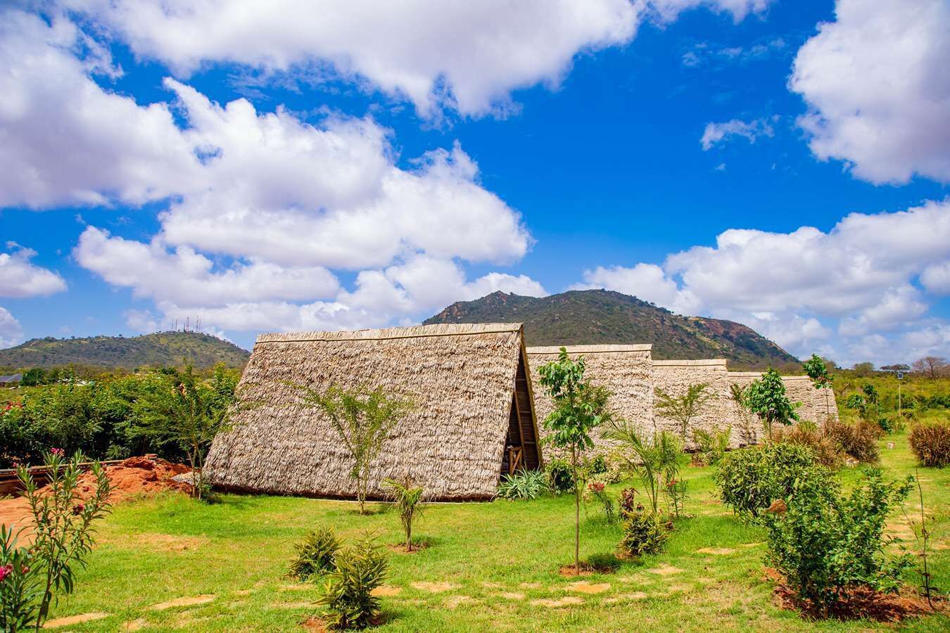 A traditional thatched-roof structure with a stone wall and a mountain in the background.