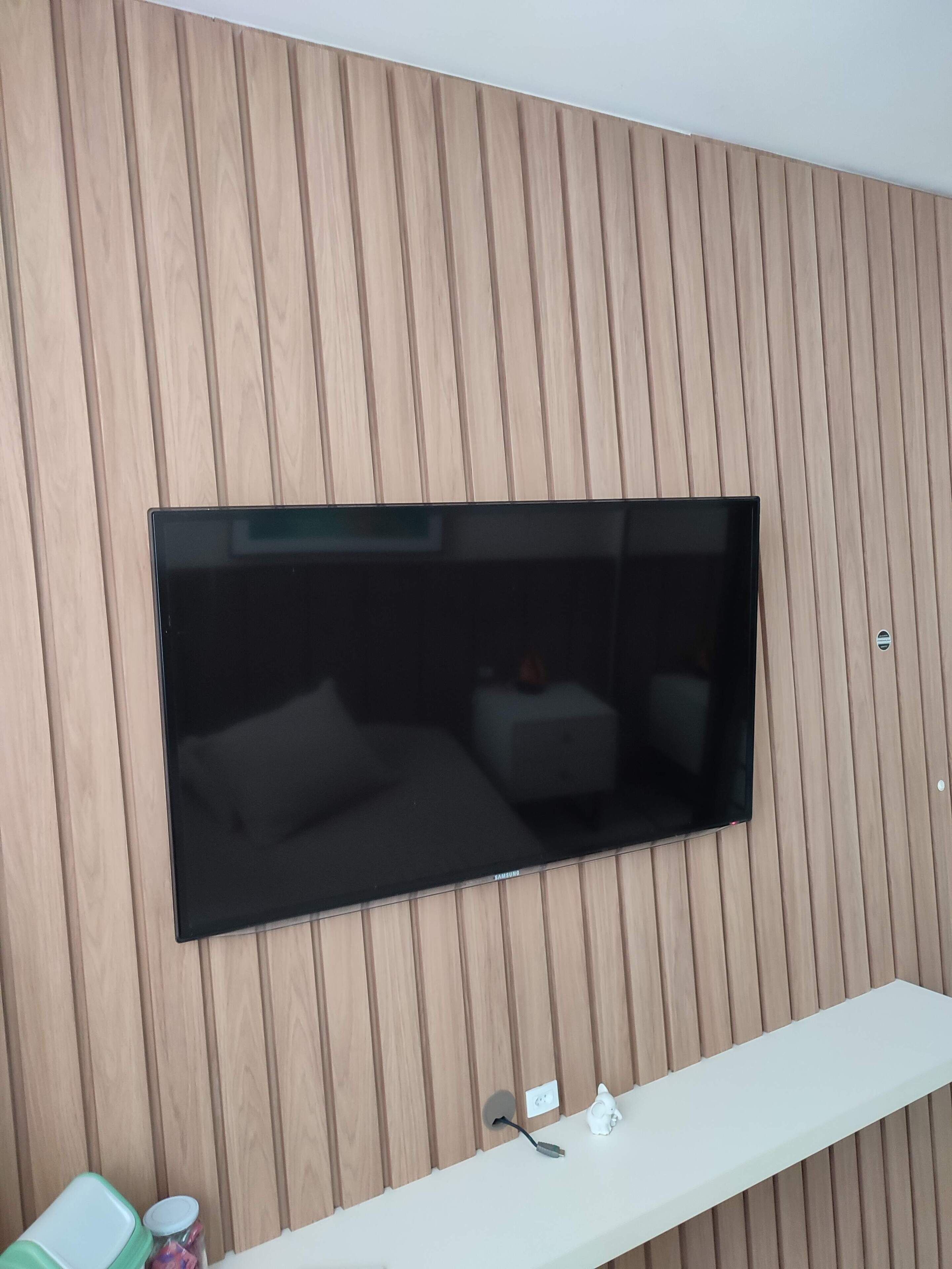 Televisor de pantalla plana montado en una pared de madera con un estante blanco debajo.