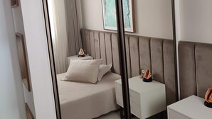 Een moderne slaapkamer met een grote spiegel, een bed met hoofdbord, een nachtkastje en een bijzettafeltje.