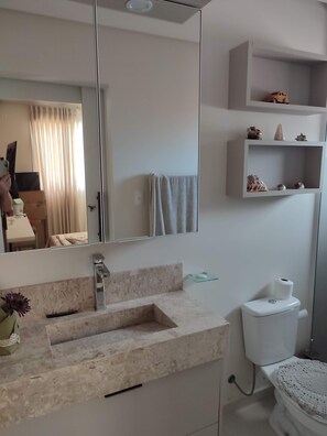 Ein modernes Badezimmer mit einem мраморный Waschbecken, einer Toilette und einem Regal mit Dekoration.