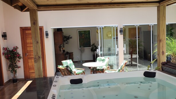 Een hottub met een houten terras en stoelen, een houten deur en een glazen deur die leidt naar een buitenruimte met planten.