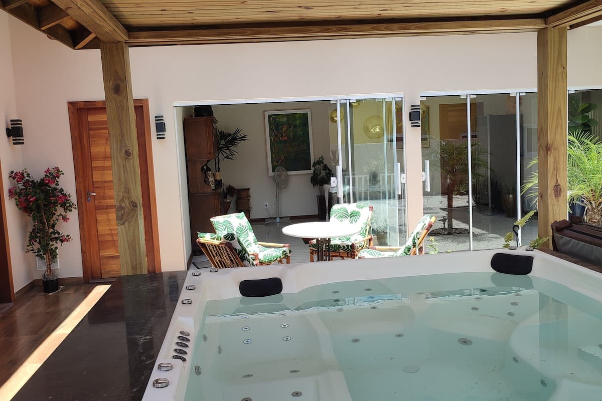 Un bain à remous doté d’une terrasse en bois et de chaises, une porte en bois et une porte en verre donnant sur un espace extérieur agrémenté de plantes.