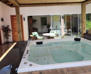 Ein Whirlpool mit einer Holzterrasse und Stühlen, eine Holztür und eine Glastür zu einem Außenbereich mit Pflanzen.