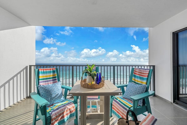 A balcony with two chairs, a table, and a view of the ocean.