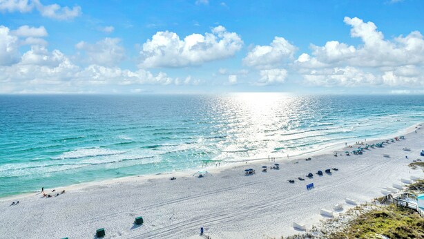 Ein Strand mit blauem Himmel, ruhiger See und einer Reihe von Liegestühlen und Sonnenschirmen.