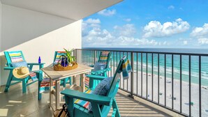 Ein Balkon mit türkisfarbenen Stühlen und einem Tisch mit Blick auf einen Strand.