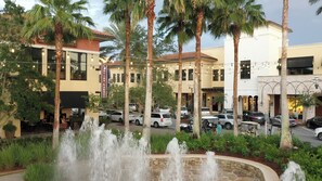 A courtyard with a fountain, palm trees, and parked cars.