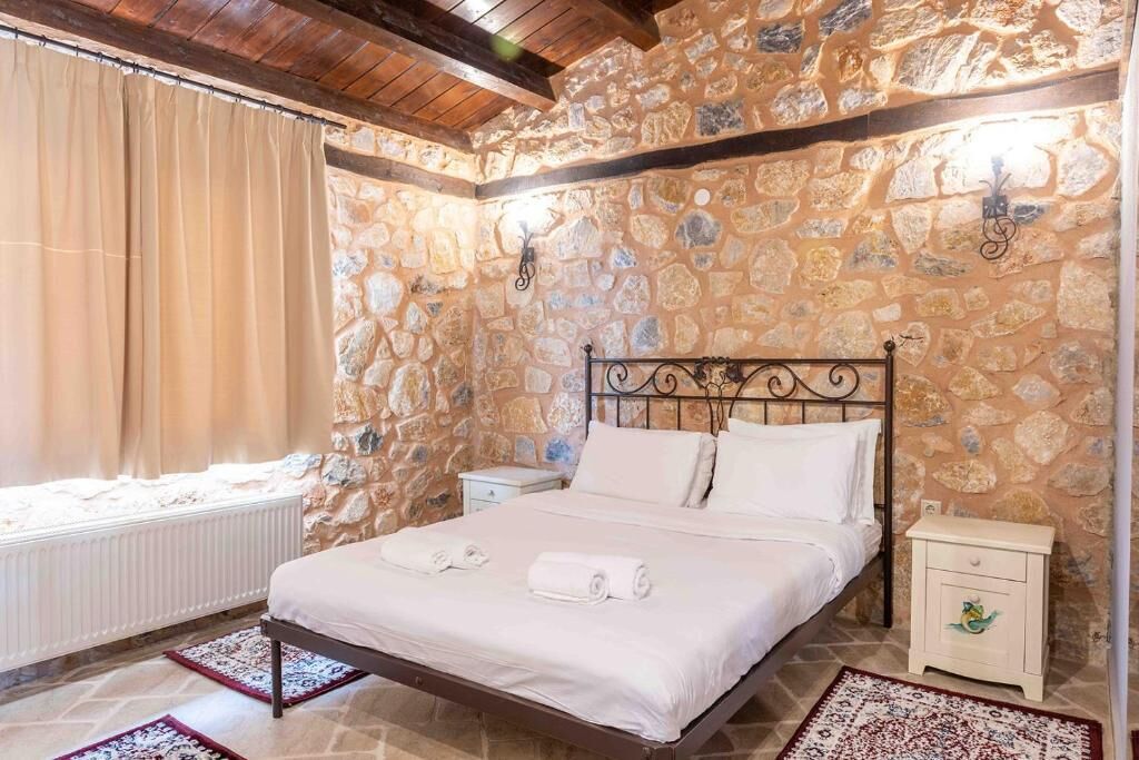 A bedroom with a stone wall, a bed with white linens, a nightstand, and a small table with a decorative item.