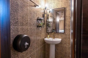 A bathroom with a patterned wall, a sink, a mirror, and a towel dispenser. - Lithea Resort (Florina)