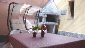 Un espace patio avec une table recouverte d’une nappe à pois, deux plantes en pot et un four en pierre.