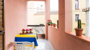 Un balcon étroit avec une table et des chaises, des plantes en pot et une vue sur les bâtiments voisins.