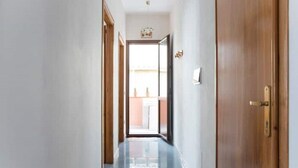 Un couloir avec une porte en bois sur la droite, un luminaire au plafond et une vue sur une pièce avec une fenêtre.