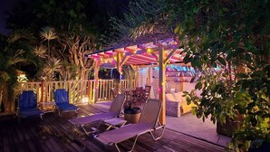Une terrasse en bois avec des chaises longues et un espace salon couvert agrémenté de guirlandes lumineuses.