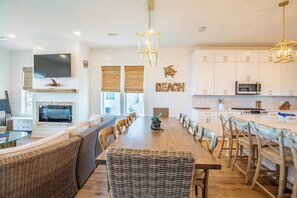 Un vaste espace de vie comprenant une grande table à manger en bois, des meubles en osier et une cheminée.