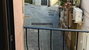 A narrow alleyway with a metal grate, a brick pathway, and a potted plant with pink flowers on the right. - ENTIRE VACATION HOME BARI SARDO Iun.gov.it Q0005 (Bari Sardo)